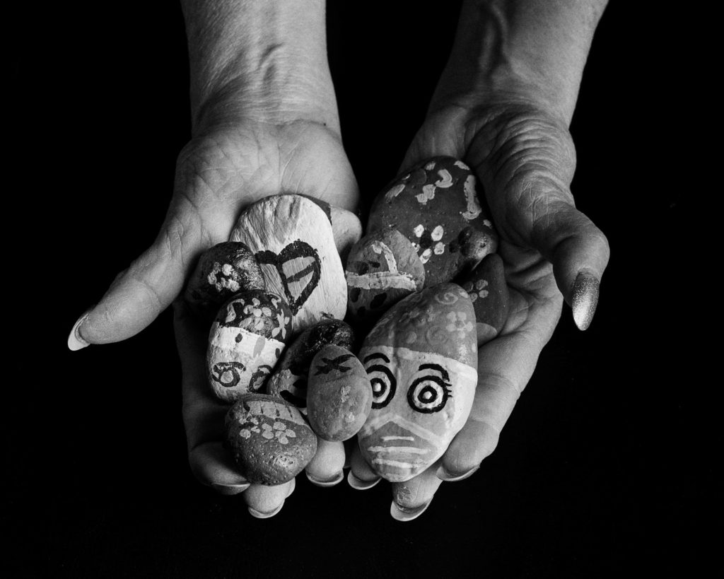 Blank and white image of a woman cupping her hands that are full of painted rocks